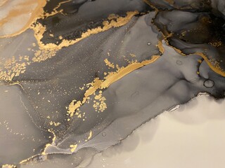 Abstract grey background with gold — beautiful smudges and stains made with alcohol ink and golden paint. Fragment of art with black and white texture resembles marble, watercolor or aquarelle.

