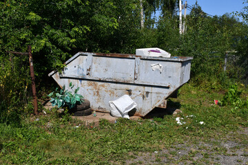 Fototapeta na wymiar a large metal container for garbage collection in a country village among green trees and bushes on a sunny day. Garbage collection. Non-shared garbage collection.