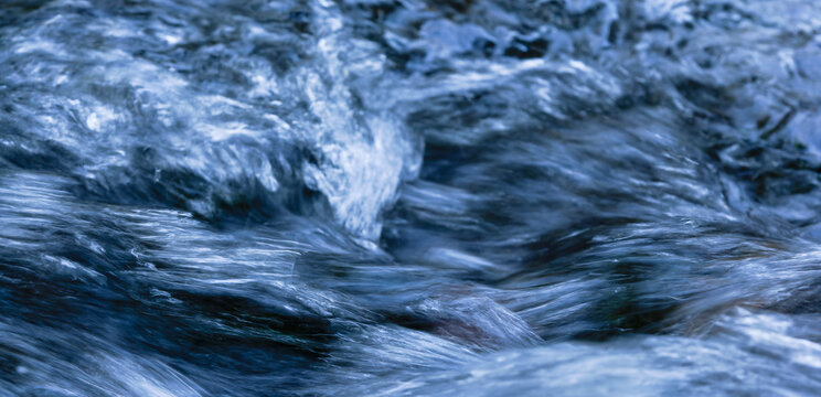 Aufgewühltes Wasser mit Schaumkrone und Gischt in weiß, hellblau, dunkelblau und schwarz als Panorama.