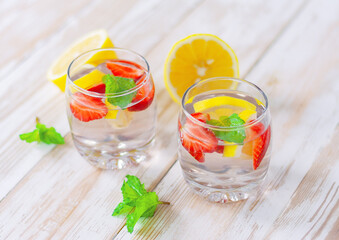 two glasses with a lemon, strawberry and mint beverage