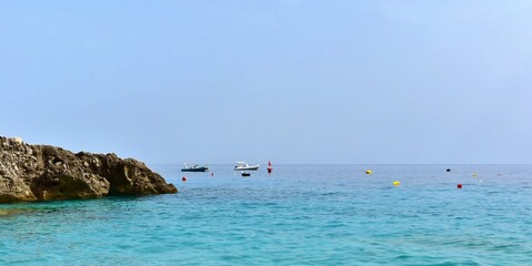 Seascape with stone coast and boats on background of blue sea and blurred horizon