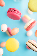 Different colors flying macaroons and chocolate eggs frozen in the air on blurred blue background. top view, close up.