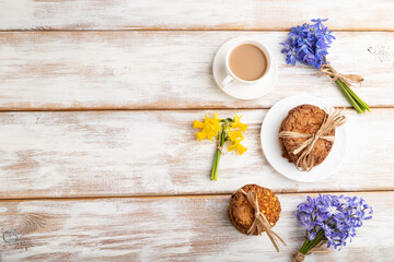 Oatmeal cookies with spring snowdrop flowers bluebells, narcissus and cup of coffee on white wooden background. top view, copy space.