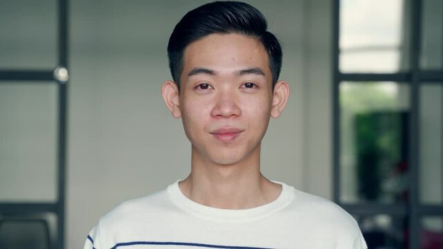 Portrait of young confident asian teen boy chinese high school college university student, IT startup worker standing in classroom office background looking at camera. Headshot. Close up.