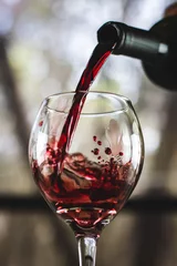 Poster Closeup shot of red wine pouring in glass isolated on blurry background © Robert Jones/Wirestock