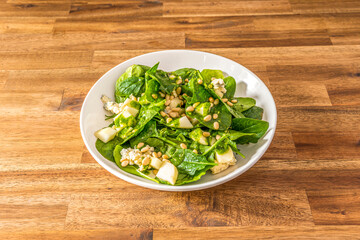 spinach salad with chopped pears, quantity of pine nuts and blue cheese in a white bowl