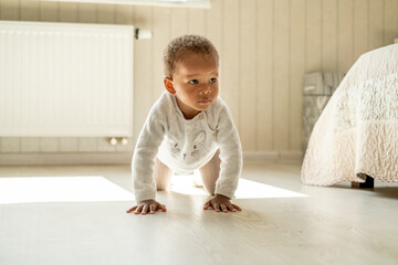 Cute persistent african american baby boy standing on his knees and hands, learning to crawling,...