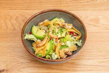 amazing shrimp salad, avocado, strips of corn chips, iceberg lettuce, lots of parsley and oil in a gray bowl with brown edge.