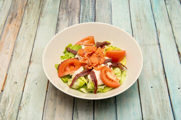 Smoked salad with Norwegian salmon, anchovies from Santoña, cheese, chopped tomato and iceberg lettuce on a white bowl