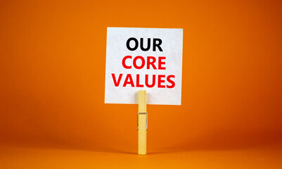 Our core values symbol. White paper with words 'Our core values', clip on wooden clothespin. Beautiful orange background. Business and our core values concept. Copy space.