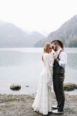 Fototapeta na wymiar The concept of a wedding. A happy married couple in love in wedding clothes hugs standing in the middle of a boat pier a lake and misty mountains in nature in a fabulously beautiful place outdoors