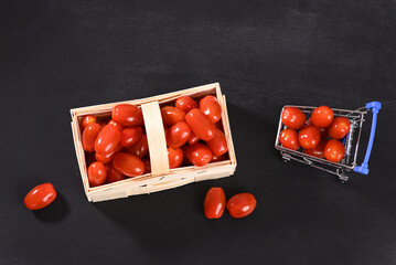 Cherry tomatoes in a wicker basket and shopping cart, top view.
