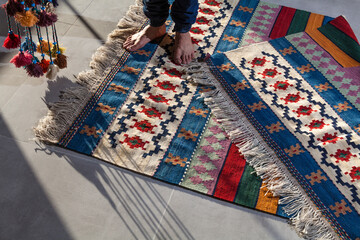 hand woven and knotted Persian kilim on the floor and a man standing on it with colorful tassels 
