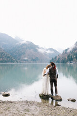 The concept of a wedding. A happy married couple in love in wedding clothes hugs standing in the middle of a boat pier a lake and misty mountains in nature in a fabulously beautiful place outdoors