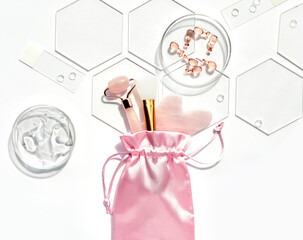 Pink quarts face roller, gua sha stone, serum capsules in chemical glass dish, hexagons. Facial...