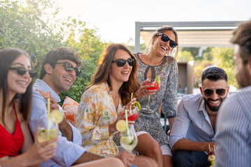 group of fashionable people drinking cocktails, young couples laughing and having fun during an...