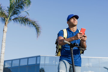 African delivery man browsing address on mobile phone map gps app for fast food order at electric scooter - Focus on courier guy face