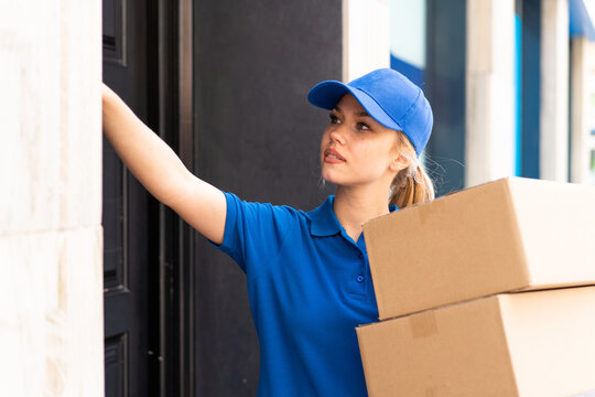 Young delivery woman at outdoors holding boxes and ringing the bell