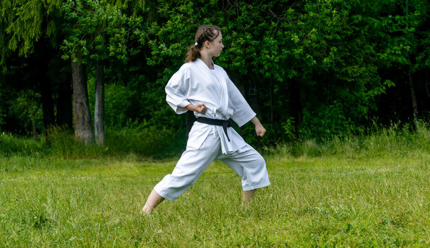 teenage girl training karate kata outdoors, performs gedan-barai or downward block