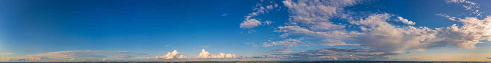 Wide panorama of blue sky with white clouds in the late afternoon.