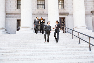 Four well dressed professionals walk down steps in discussion outside of a courthouse or municipal...
