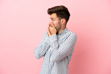 Young caucasian handsome man isolated on pink background covering mouth and looking to the side