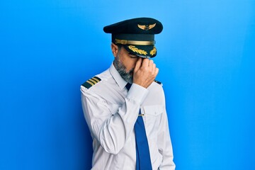 Middle age man with beard and grey hair wearing airplane pilot uniform tired rubbing nose and eyes feeling fatigue and headache. stress and frustration concept. © Krakenimages.com