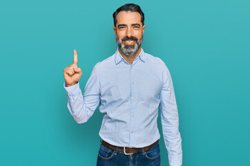 Naklejka premium Middle aged man with beard wearing business shirt showing and pointing up with finger number one while smiling confident and happy.