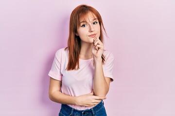 Redhead young woman wearing casual pink t shirt looking confident at the camera with smile with crossed arms and hand raised on chin. thinking positive.