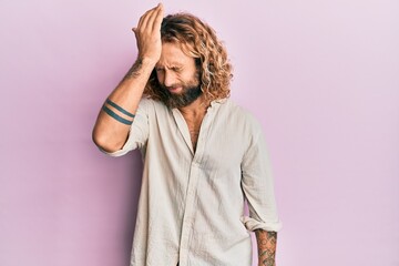 Handsome man with beard and long hair wearing casual clothes surprised with hand on head for mistake, remember error. forgot, bad memory concept.