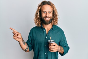 Handsome man with beard and long hair drinking mate infusion smiling happy pointing with hand and...