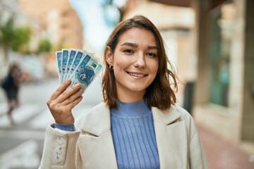 Young hispanic woman smiling happy holding polish zloty banknotes at the city