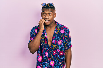 Young black man wearing hawaiian shirt and sunglasses looking stressed and nervous with hands on mouth biting nails. anxiety problem.