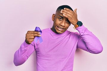 Young black man holding purple ribbon awareness stressed and frustrated with hand on head,...