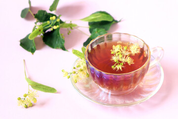The concept of taking medicinal herbal teas.A cup of tea with linden flowers, green branches on a light background, side view.