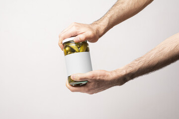 Closeup of male hands opening pickled cucumber jar with white blank label - editable mockup template