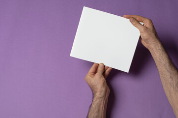 Male hands holding a catalog with blank cover on purple background - editable mockup template