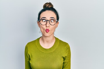 Young hispanic girl wearing casual clothes and glasses making fish face with lips, crazy and comical gesture. funny expression.
