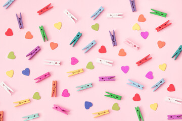 Small colorful wooden laundry tongs with colorful wooden hearts arranged on a pink background..