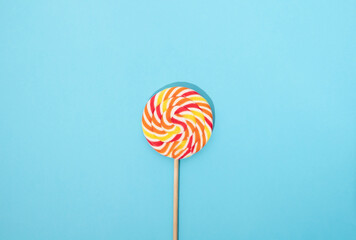 Colorful round lollipop with wooden handle on a blue background.