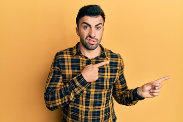 Young hispanic man wearing casual clothes pointing aside worried and nervous with both hands, concerned and surprised expression