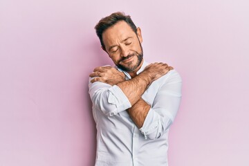 Middle age man wearing casual clothes hugging oneself happy and positive, smiling confident. self...