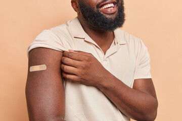 Cropped shot of unrecognizable man with thick beard shows arm with plaster glad to be vaccineted...