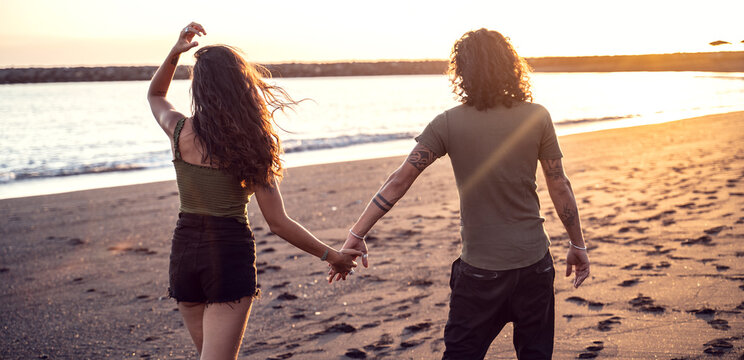 Beautiful beach couple watching sunset together, holding hands.