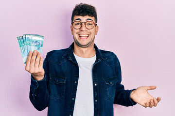 Young hispanic man holding 50 malaysia ringgit banknotes celebrating achievement with happy smile...
