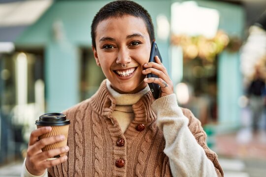 Young hispanic woman with short hair smiling happy drinking a cup of coffee and talking on the phone