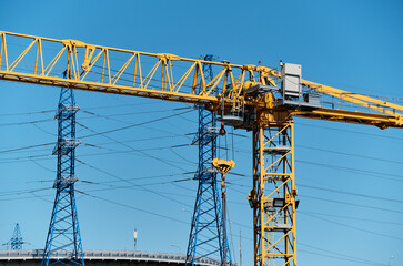 Yellow construction crane boom on the background of power transmission towers and road junctions