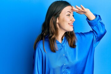 Young brunette woman wearing casual blue shirt very happy and smiling looking far away with hand over head. searching concept.