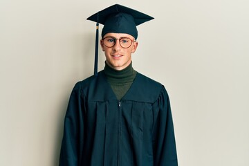 Young caucasian man wearing graduation cap and ceremony robe with a happy and cool smile on face. lucky person.