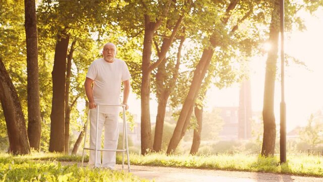 Disabled old man is walking with a walker. Handicapped patient in the park. Assistance, rehabilitation and health care. Golden hour sunset.